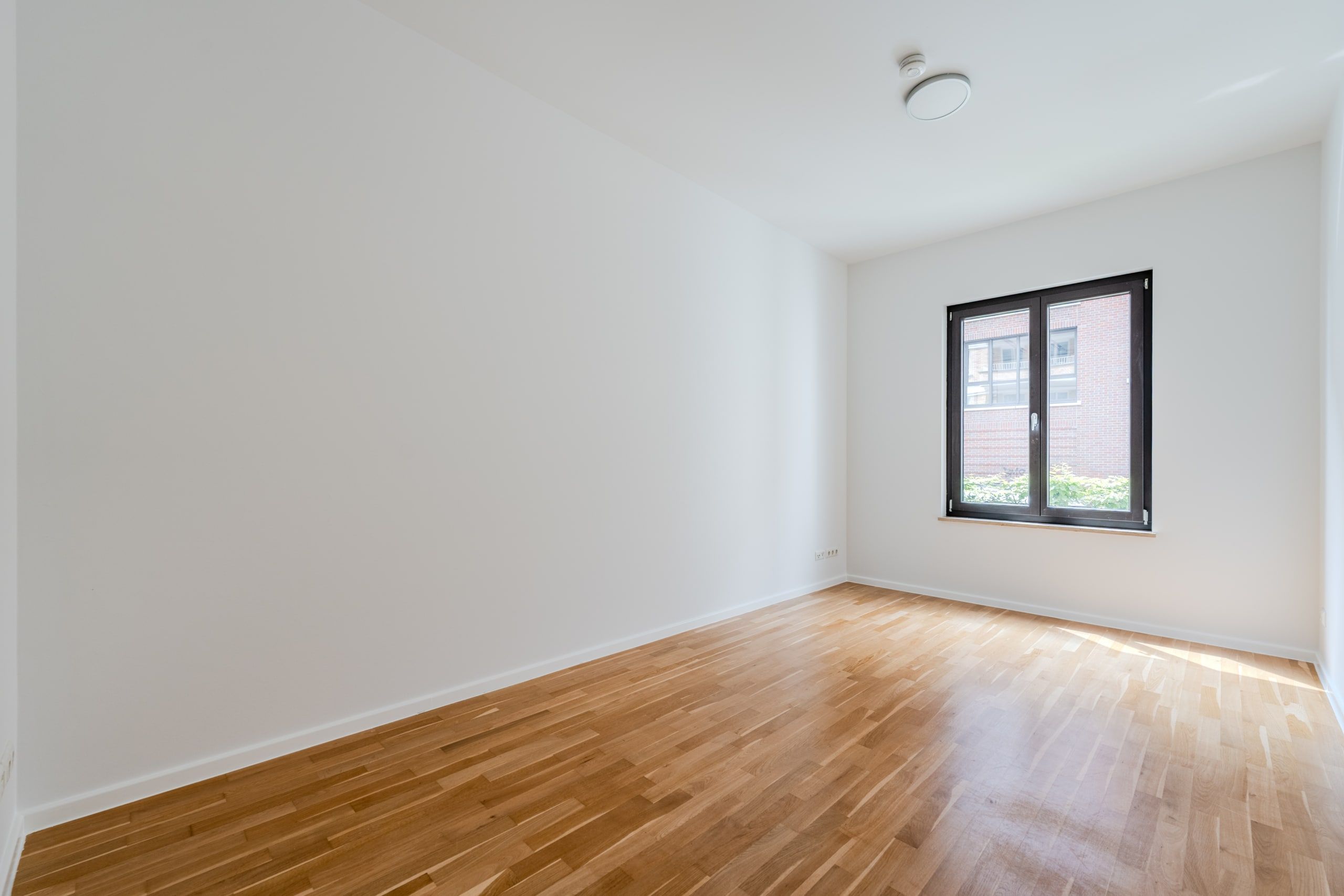Leerstehendes Zimmer mit hellem Parkettboden Innenperspektive weiße Wände Rauchmelder an Decke Fenster zur Klinkerfassade
