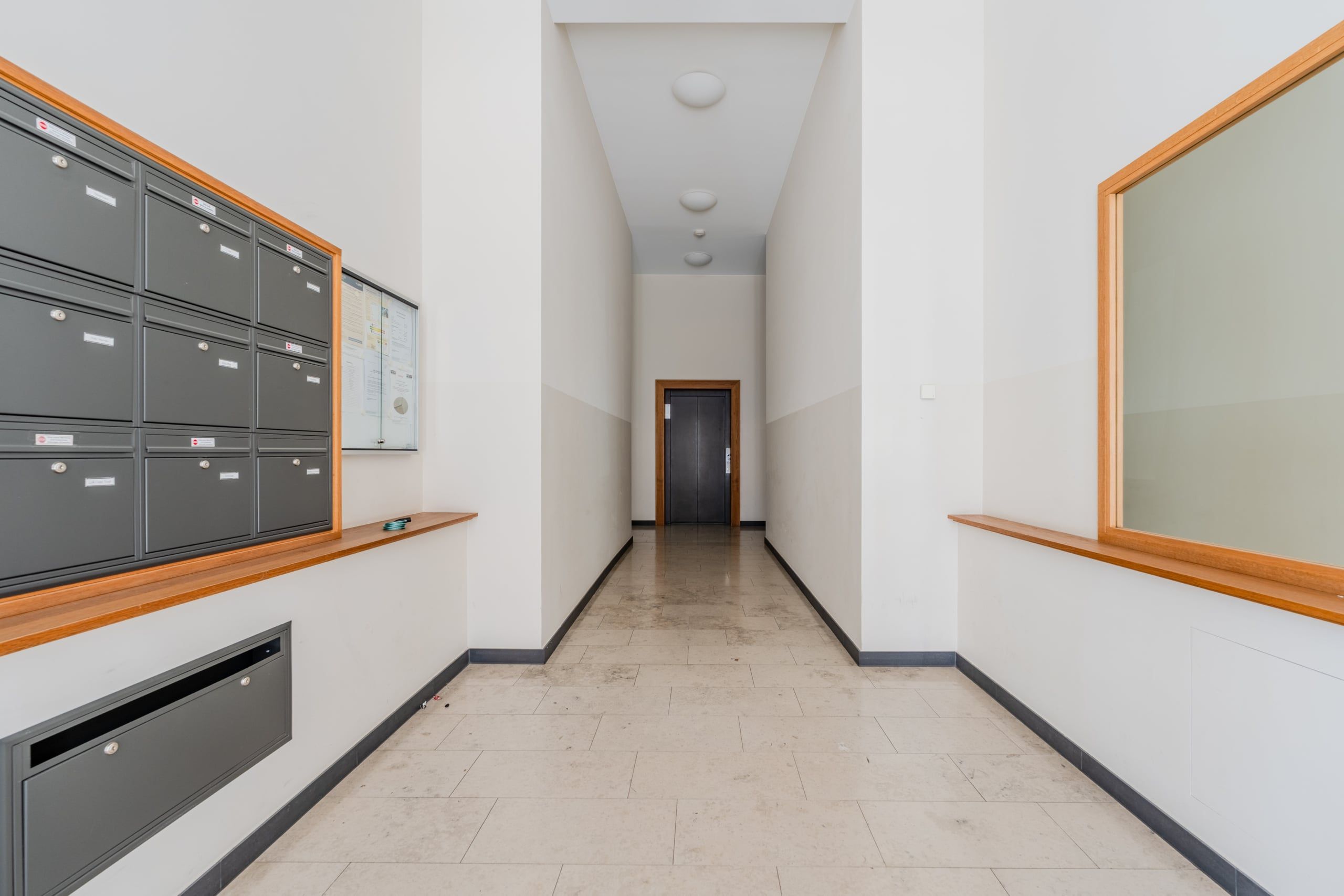 Wohnungshausflur mit grauen Briefkästen links Fenster mit Holzrahmen rechts Blick auf schwarzen Fahrstuhl