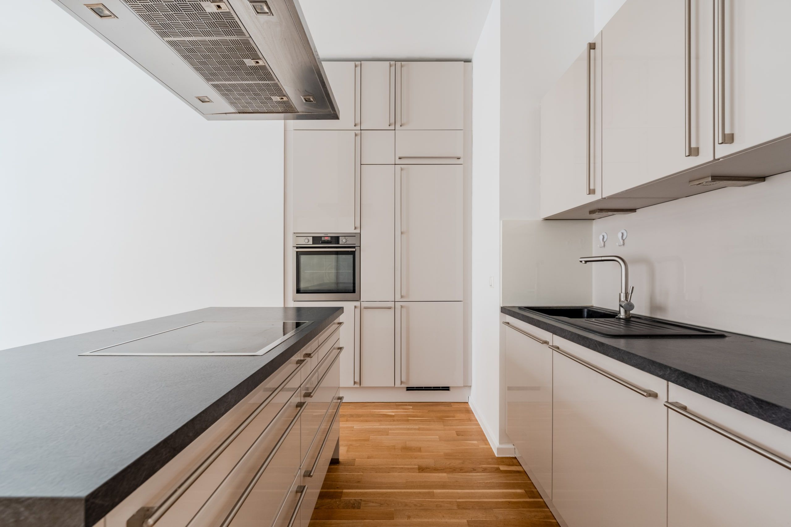 Frontale Sicht auf Küchenbereich einer Neubauwohnung mit Kochinsel, weißen Hochglanzfronten und Parkettboden