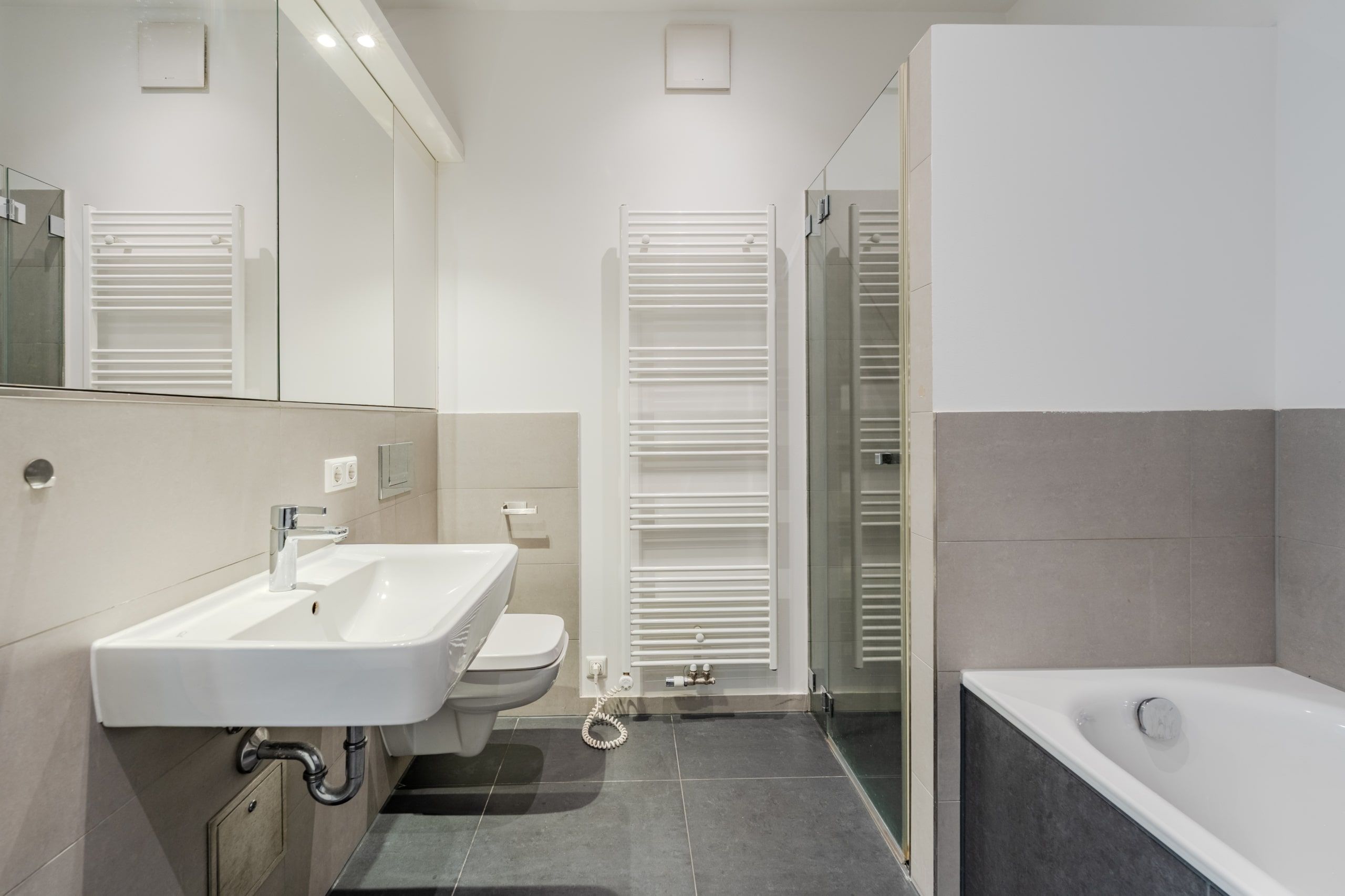 Innenansicht eines modernen Badezimmers mit Badewanne, Glasdusche, Wandwaschbecken, Toilette und Handtuchheizkörper