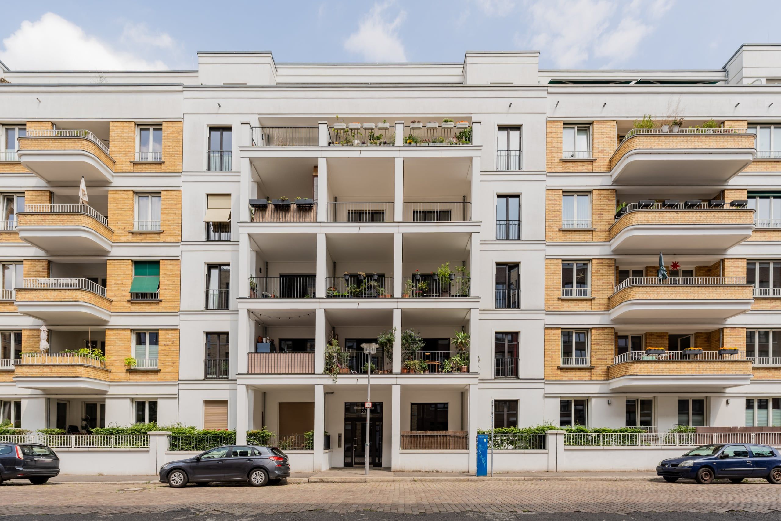 Fünfgeschossiges Mehrfamilienhaus mit weißer Putz- und gelber Klinkerfassade und Balkonreihen in Straßenansicht