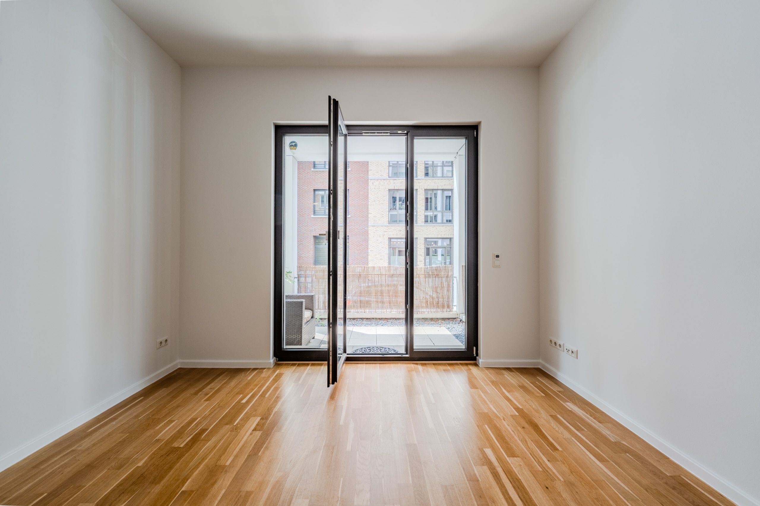 Innenansicht Neubauwohnung mit Parkettboden und bodentiefer Glastür zum Balkon