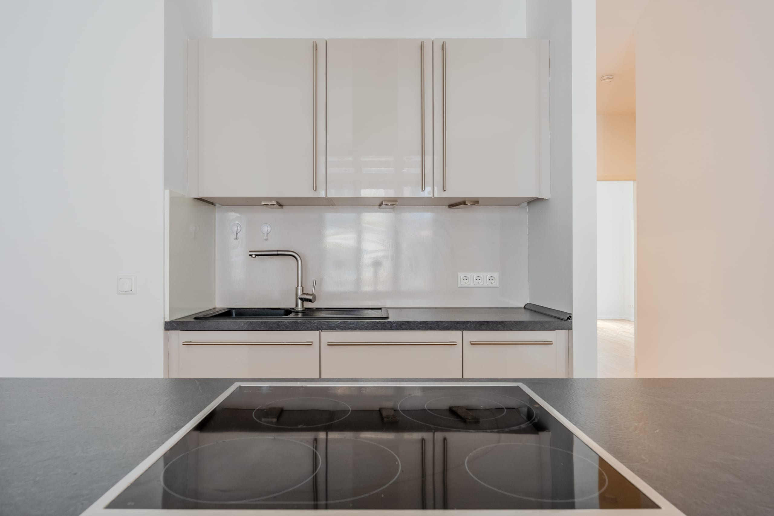 Moderne Einbauküche in Neubauwohnung mit Kochinsel Cerankochfeld und Hochglanzschränken aus Frontalperspektive