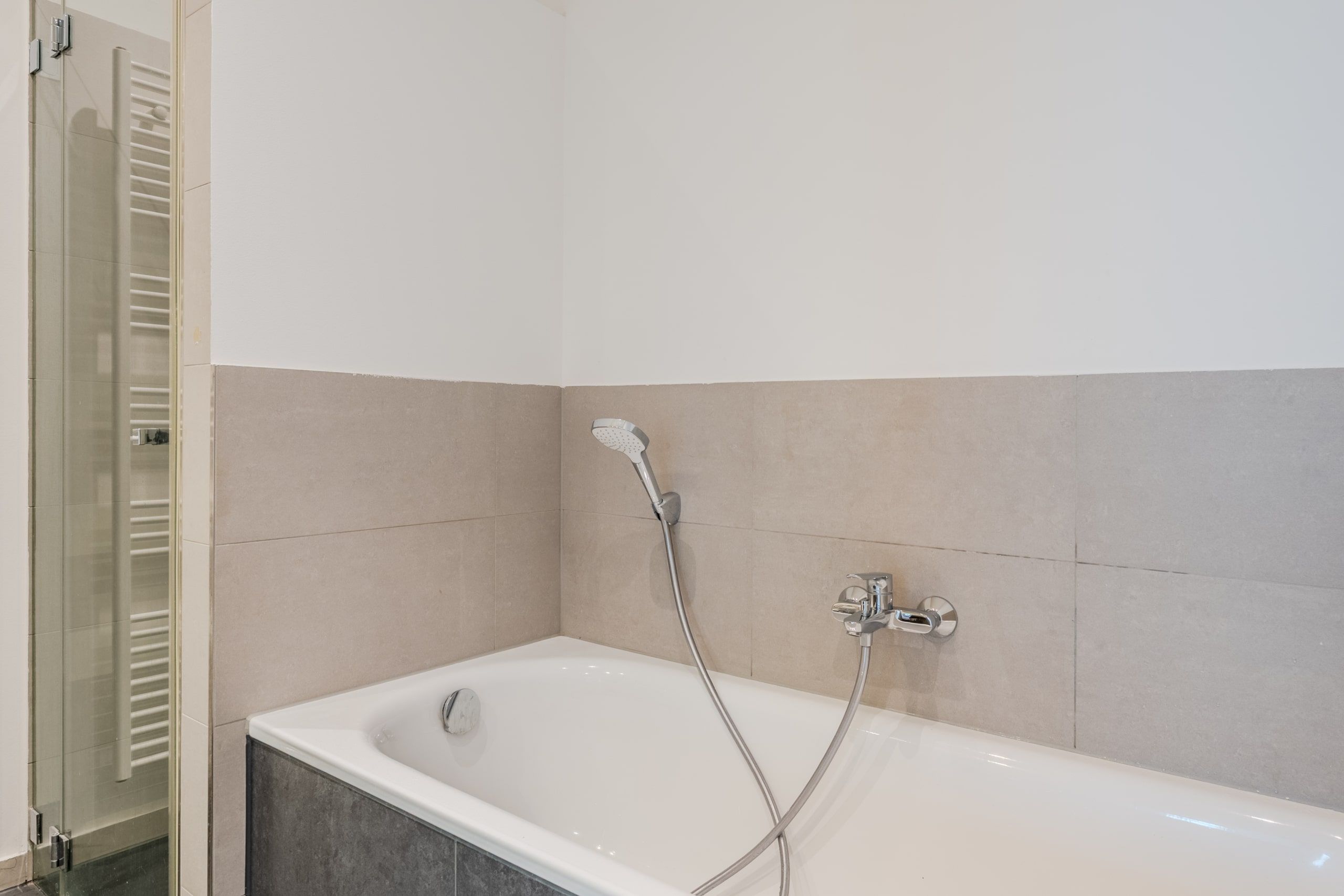Innenansicht modernes Badezimmer mit eingelassener Wanne Handbrause Glasduschabtrennung und halbhohen beigen Fliesen