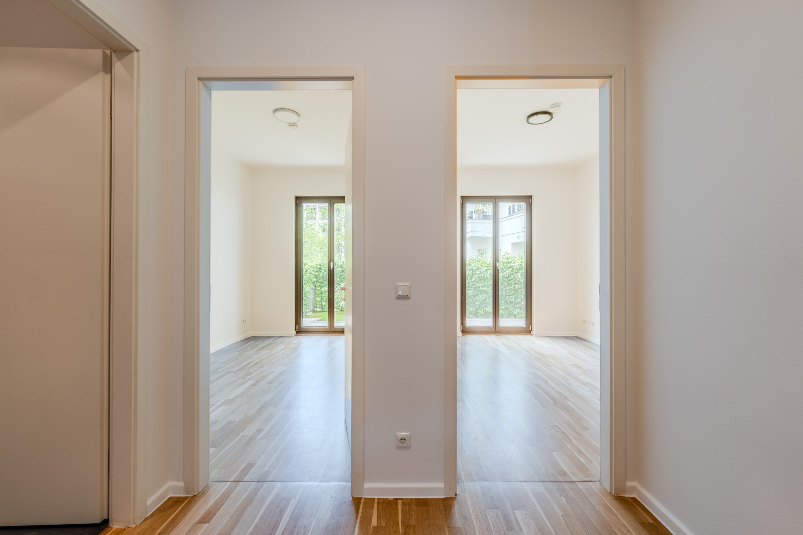 Blick durch Flur auf zwei lichthelle Räume mit Parkettboden und bodentiefen Fenstertüren zum Garten