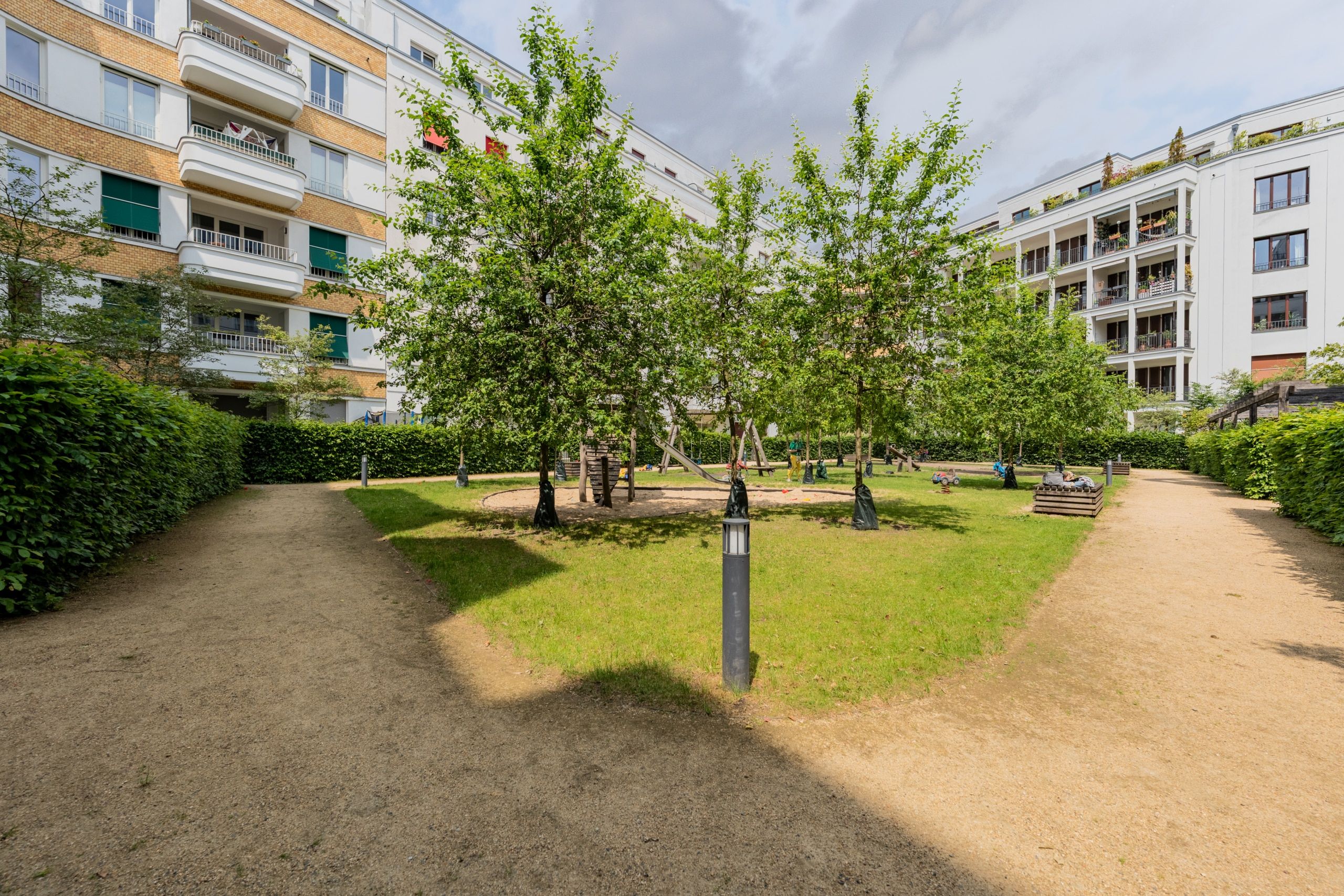 Blick in den begrünten Innenhof eines Mehrfamilienhauses mit Spielplatz, Spazierweg und umlaufenden Balkonen
