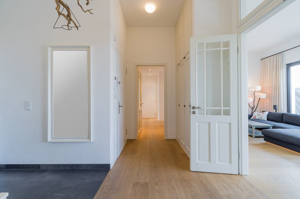 Heller Wohnungsflur mit Eichenparkett Blick durch offene weiße Türen ins Wohnzimmer mit grauem Ecksofa und Stehlampe
