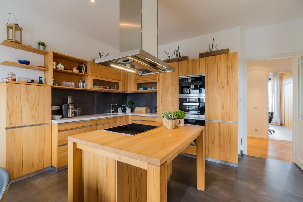 Interieur einer offenen Wohnküche mit Holzinsel frontal mit Edelstahl Dunstabzugshaube und Eckschränken in modernem Stil