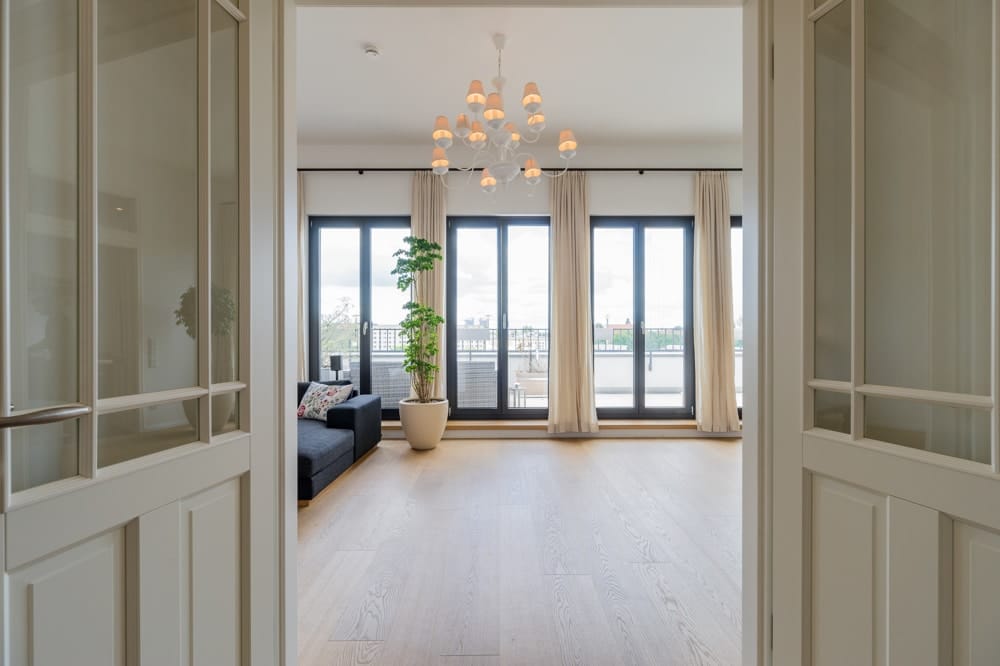 Blick durch offene Doppeltür in modernes Wohnapartment mit Parkettboden bodentiefen Fenstertüren und Balkon