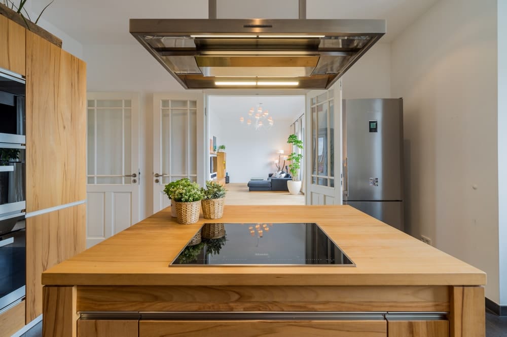 Offene Küche mit Holzinsel und Dunstabzug über Induktionskochfeld Blick in Wohnbereich mit Sofa
