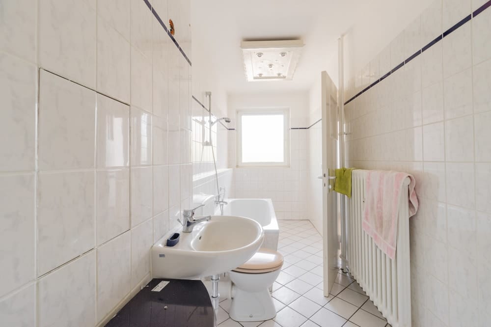 Innenansicht Badezimmer aus Türöffnung mit Badewanne Waschbecken WC Handtuchheizkörper und Fliesenboden