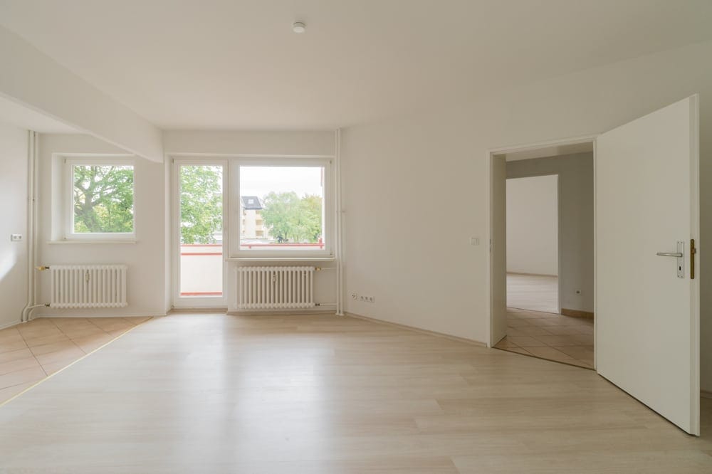 Innenansicht leerer Wohnung mit hellem Laminatboden Balkonzugang und weißen Wänden