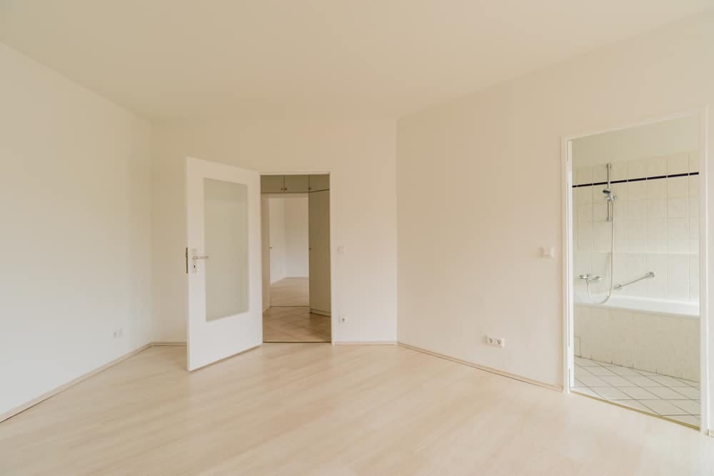 Innenansicht leerer Wohnung mit Laminatboden offene Tür zum gefliesten Bad mit Badewanne und Duscharmatur