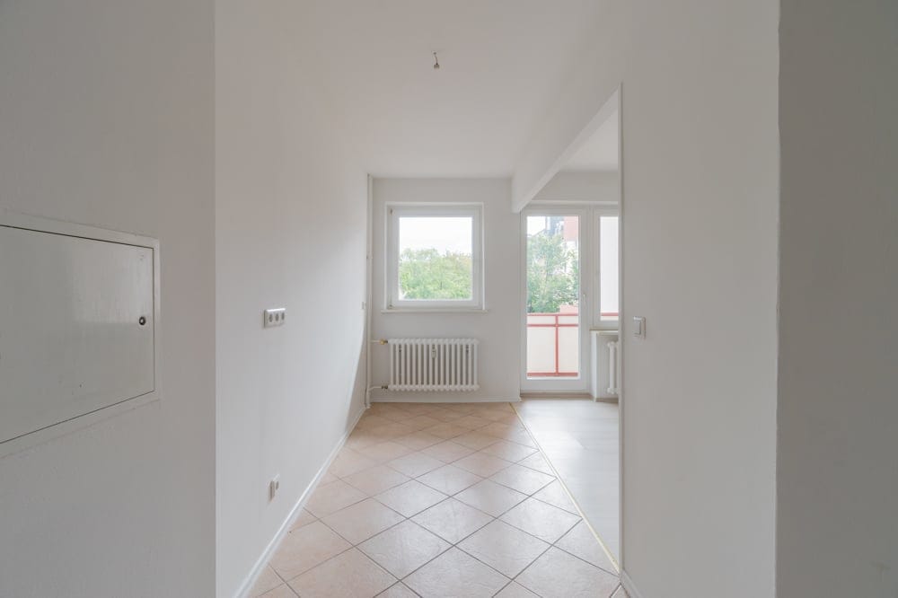 Innenansicht einer hellen Wohnung mit Fliesenboden Radiator Fenster und Balkonzugang aus Flurperspektive