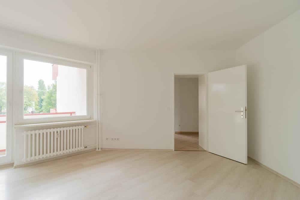 Innenansicht helle Wohnung mit Laminatboden Balkonfenster Heizkörper und offener Zimmertür