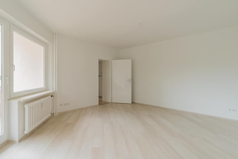 Leerer Wohnraum in moderner Neubauwohnung frontal mit Fenster, Heizkörper und offenem Durchgang zum Flur