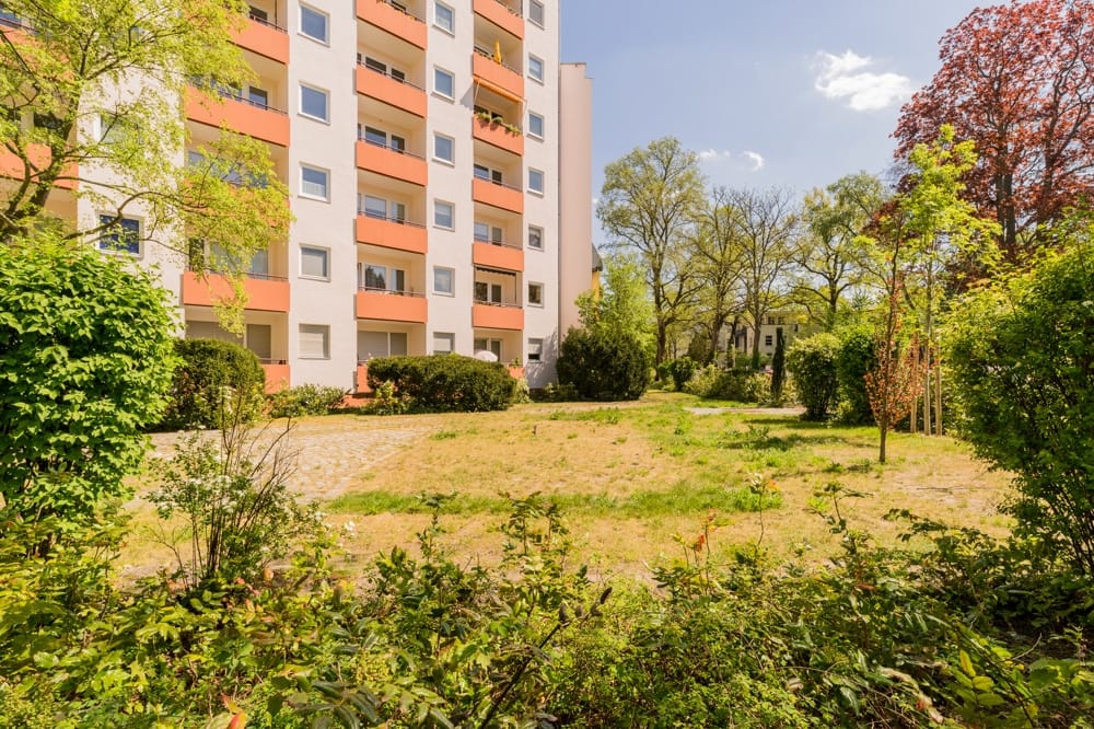 Frontansicht eines mehrgeschossigen Wohnhauses mit orangefarbenen Balkonen und Vorgarten
