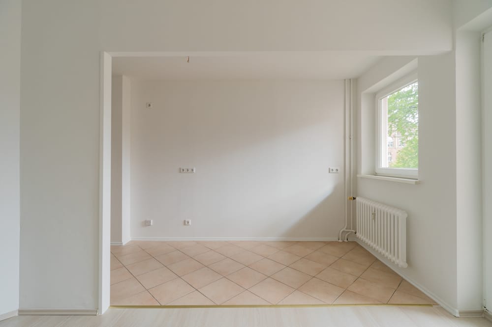 Blick in eine helle Wohnung mit offener Wohnküche, beigem Fliesenboden und Heizkörper unterm Fenster