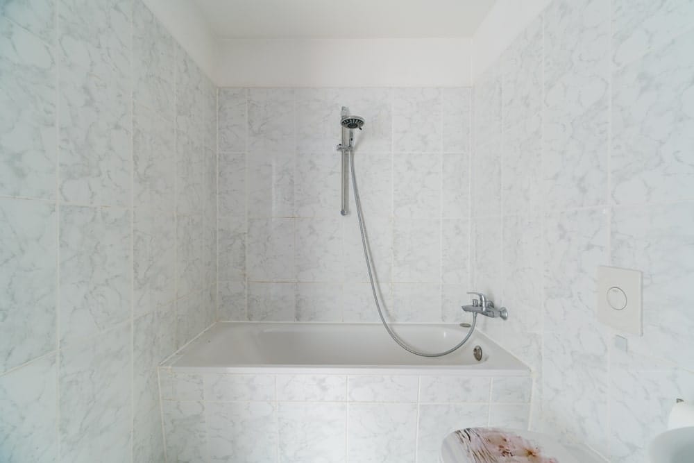 Badezimmer mit weißer Marmorfliesenwand und Badewanne mit Handbrause