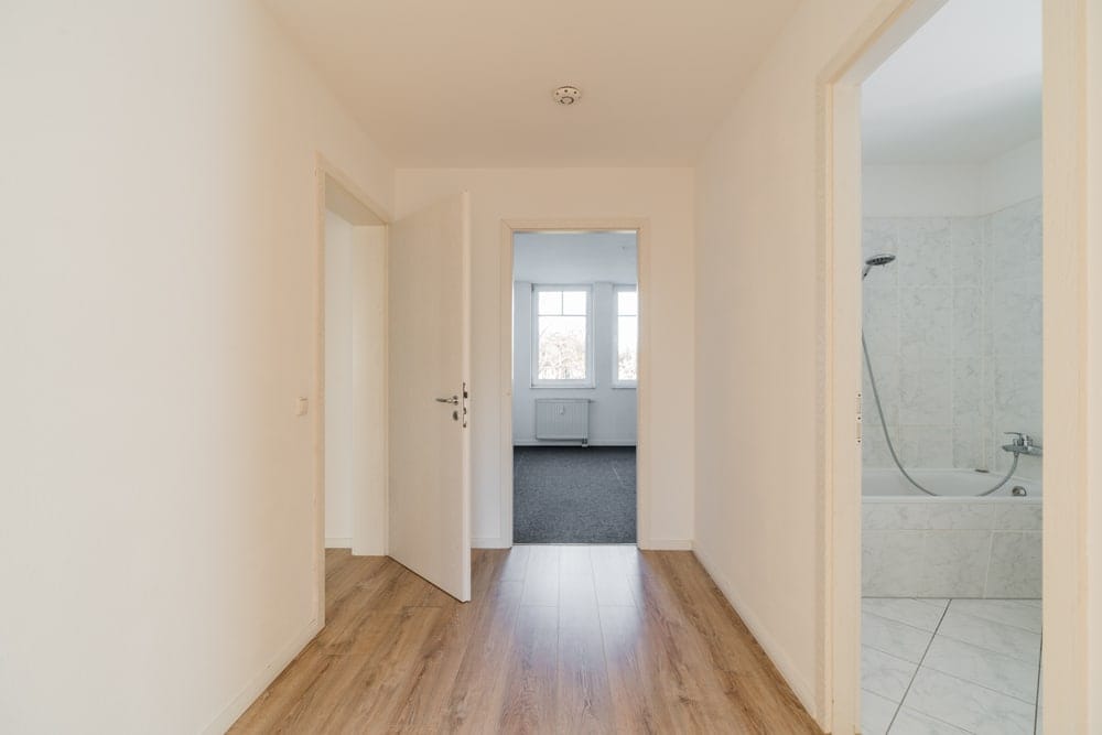 Innenansicht Flur mit Laminatboden Blick ins geflieste Bad mit Badewanne und ins Zimmer mit Teppichboden und Fenster