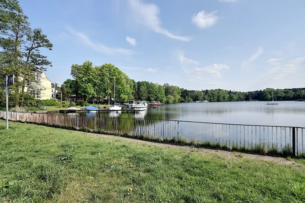 Seitenansicht auf ein Wohngebäude am Seeufer mit Steg und Bootsliegeplätzen vor Waldkulisse