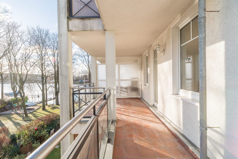 Wohnungsbalkon mit Terrakottaboden und Glasbalustrade aus Perspektive entlang des Flussufers und Gartenblick