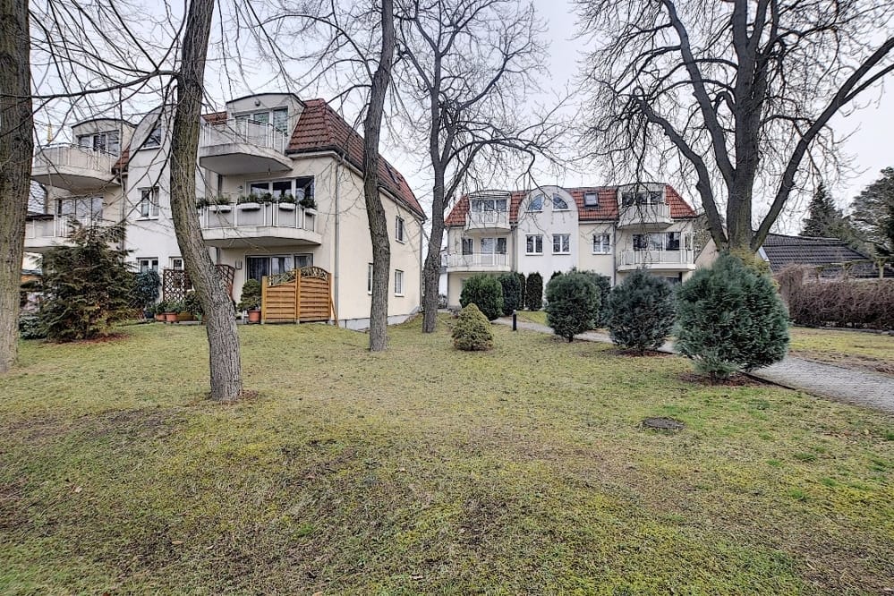 Vue de face de deux immeubles collectifs blancs de trois étages, dotés de toits mansardés rouges et de balcons donnant sur une pelouse arborée