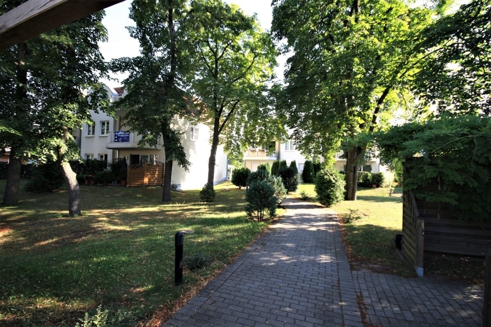 Immeuble collectif doté de balcons lumineux, offrant une vue dégagée le long d'un chemin pavé et sur les jardins environnants