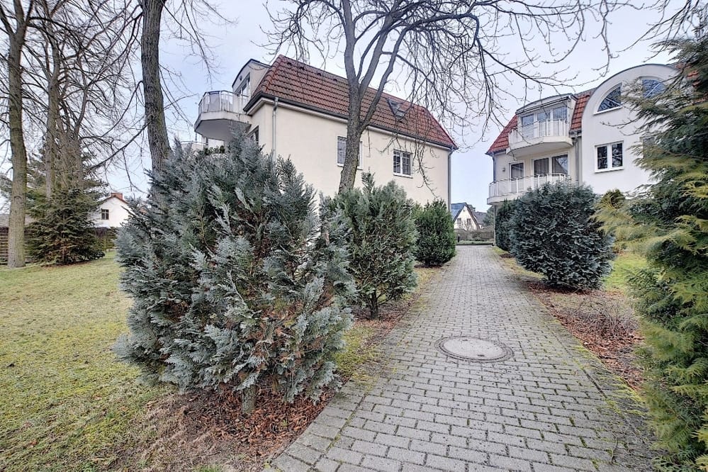 Deux immeubles d'habitation aux toits rouges et dotés de balcons, situés le long d'une allée pavée et entourés de haies