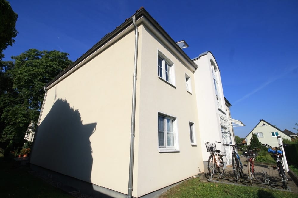 Immeuble collectif de deux étages avec une façade en crépi blanc et des vélos devant l'entrée, vu en perspective d'angle