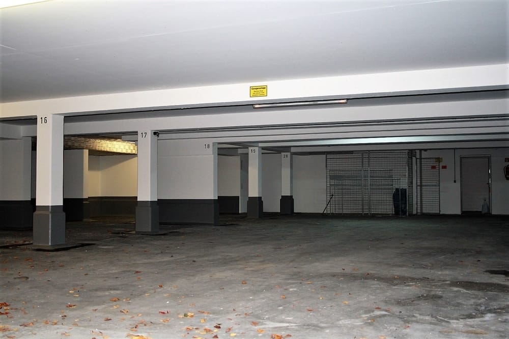 Vue intérieure d'un parking souterrain lumineux, avec des places de stationnement numérotées, des piliers de soutien gris et un sol en béton