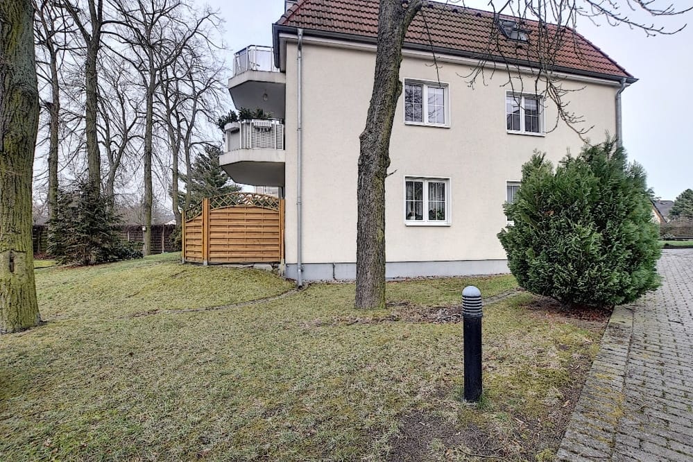 Vue de face d'un immeuble collectif avec une façade en crépi, un toit en tuiles rouges, deux balcons et un petit jardin devant la maison