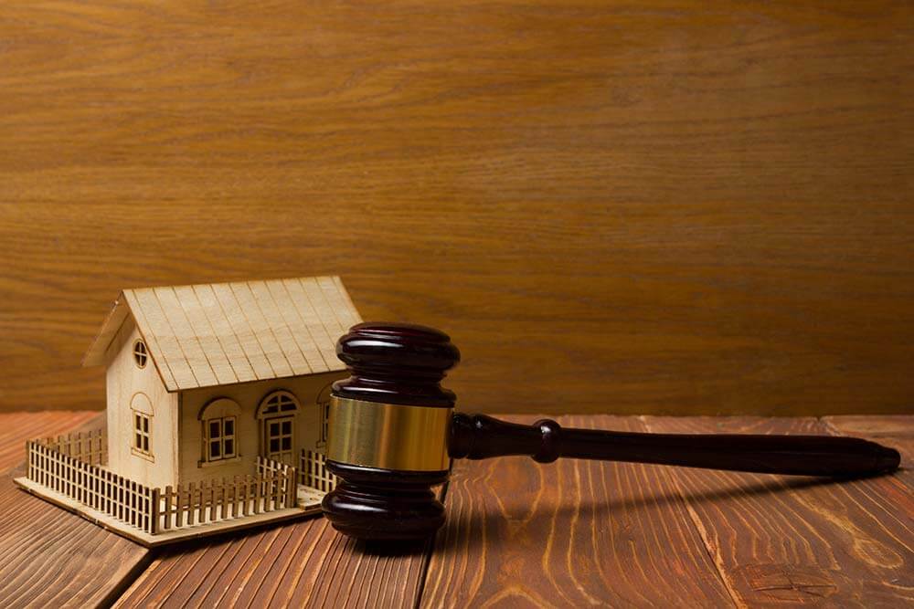 Holzmodell eines Einfamilienhauses in Frontansicht mit kleiner Umzäunung neben Richterhammer auf Holzuntergrund