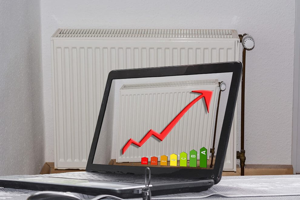 Interior view of living room frontal on white radiator with thermostat next to laptop with ascending energy efficiency diagram
