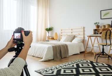 Binnenzicht van een lichte slaapkamer met tweepersoonsbed en houten lattenbodem, evenals een bureau, planten en tapijt