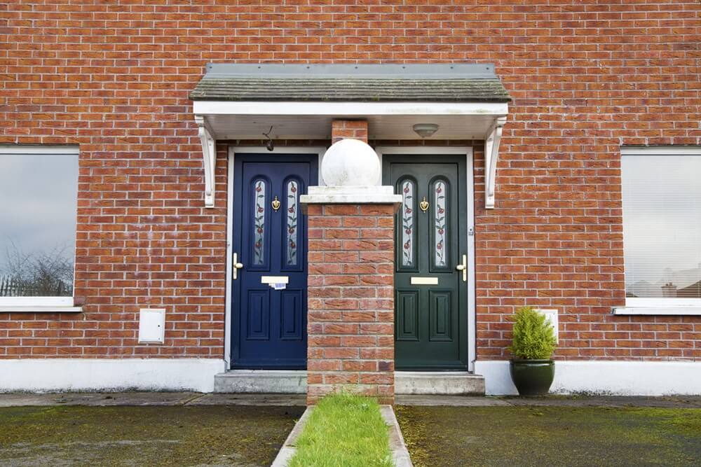 Front view of a two-storey semi-detached house with clinker brick façade and two colourful front doors under a canopy