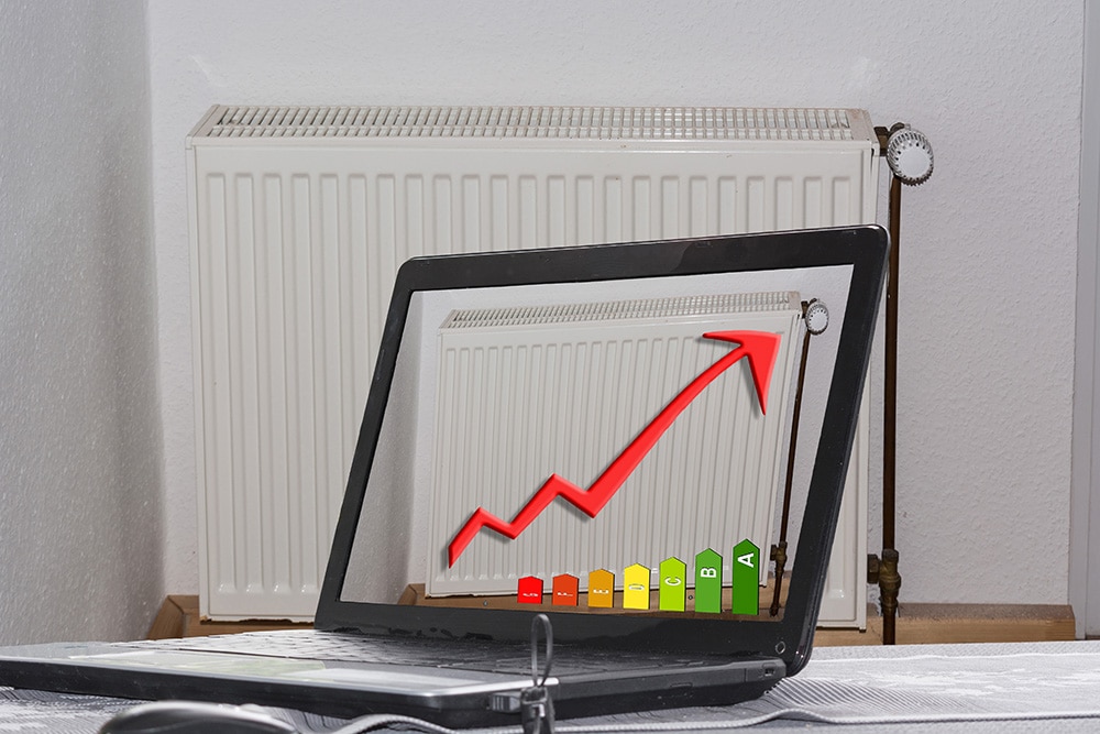 Vista frontal de un radiador delante de una pared de color claro con portátil abierto y diagrama de eficiencia energética con flecha roja