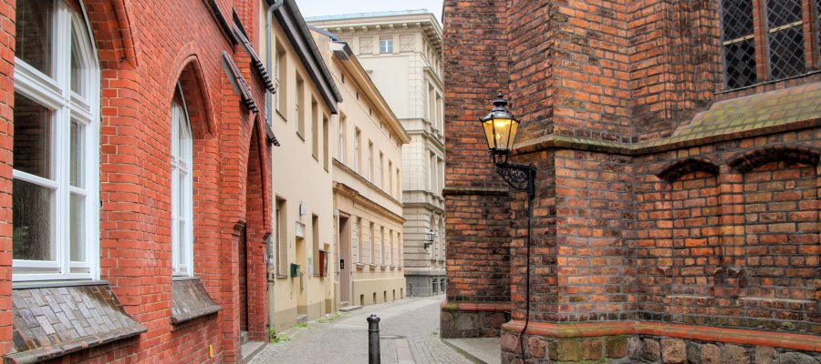 Smalle steeg met kinderkopjes tussen rode bakstenen gevels en beige pleistergevel met historische muurlantaarn