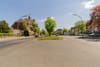 Straßenansicht eines zweigeschossigen Backsteinhauses mit kleinem Turm und begrünten Mittelstreifen