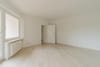 Leerer Wohnraum in moderner Neubauwohnung frontal mit Fenster, Heizkörper und offenem Durchgang zum Flur