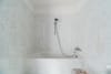 Badezimmer mit weißer Marmorfliesenwand und Badewanne mit Handbrause