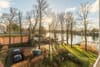 Ausblick von Balkon auf Hauszufahrt mit Parkplatz, Baumbestand und Flussufer mit Bootssteg