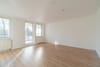 Leeres Apartmentwohnzimmer aus Eckperspektive mit Laminatboden großen Fenstern und Balkonzugang