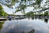 Bootshafen mit Stegen und Segel- und Motorbooten auf ruhigem See vor grüner Uferkulisse