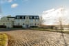 Frontansicht einer dreigeschossigen Villa mit Mansarddach, kopfsteinpflaster und Blick auf Seeufer