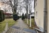 Blick entlang eines gepflasterten Wegs im Innenhof eines Mehrfamilienhauses mit Briefkästen und immergrünen Hecken