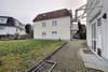 Frontansicht eines zweigeschossigen Mehrfamilienhauses mit rotem Satteldach Balkon und Vorgarten mit Fahrradständer