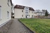 Dreigeschossiges Mehrfamilienhaus mit hellem Putz, rotem Ziegeldach, mittigem Bogenfenster und Vorgarten mit Rasen