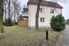 Vorderansicht eines Mehrfamilienhauses mit Putzfassade rotem Ziegeldach zwei Balkonen und kleinem Vorgarten