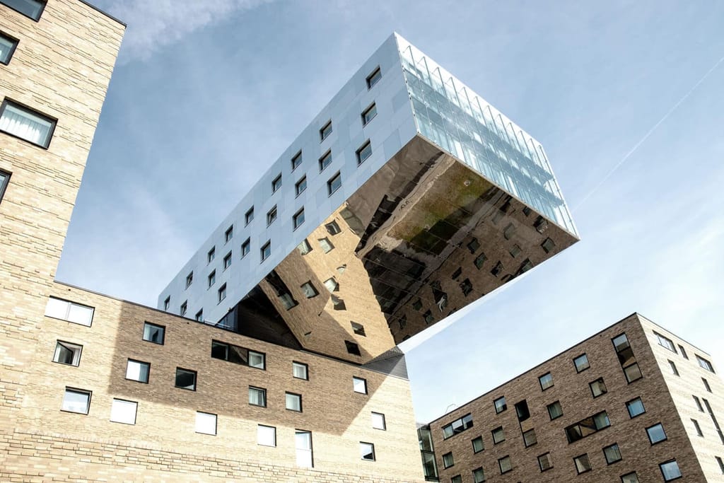 Onderaanzicht van modern flatgebouw met gevel van baksteen en overhangende spiegelende bovenverdieping van glas